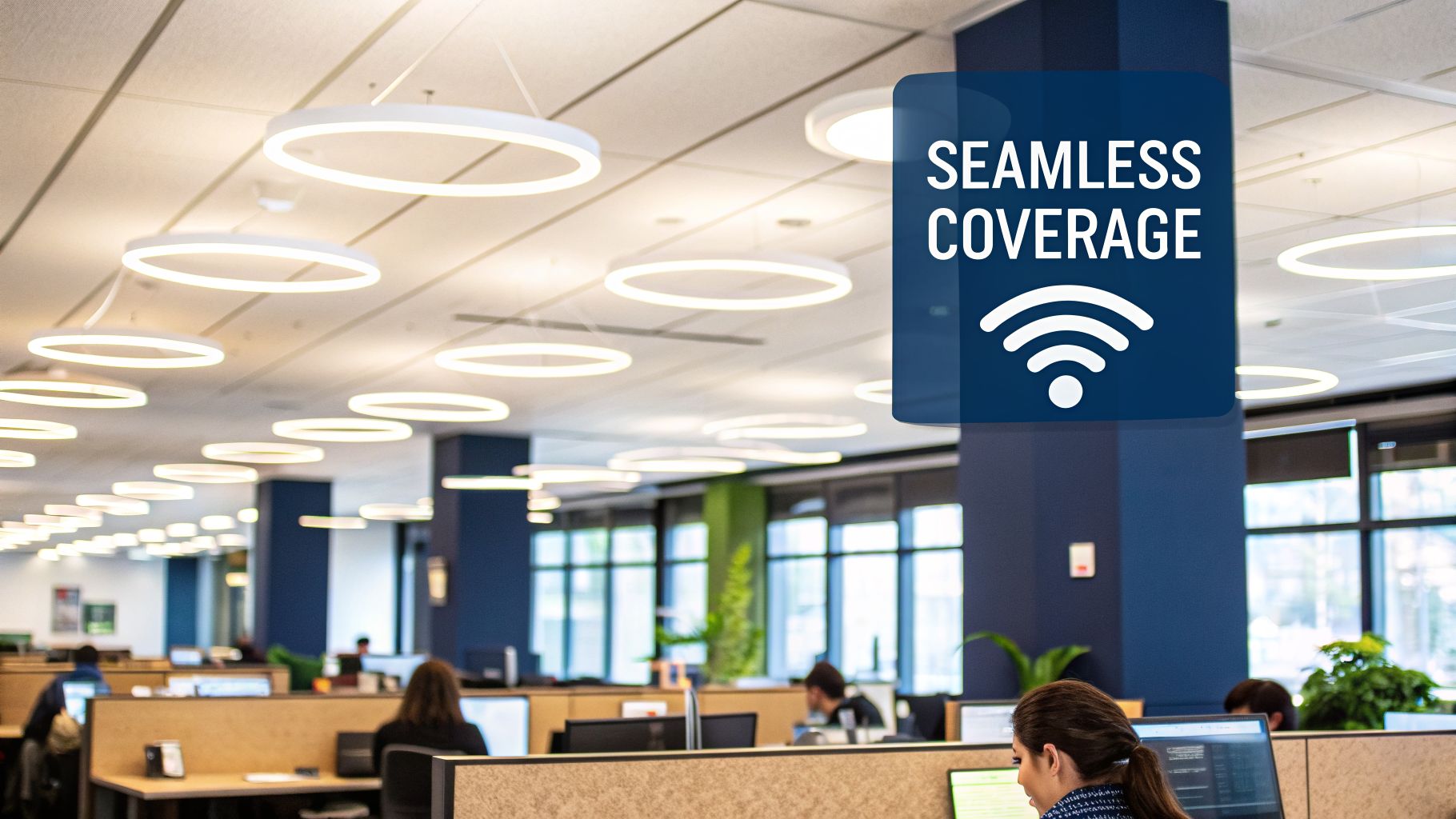 An open-plan office with employees working at desks, featuring a 'Seamless Coverage' Wi-Fi overlay.