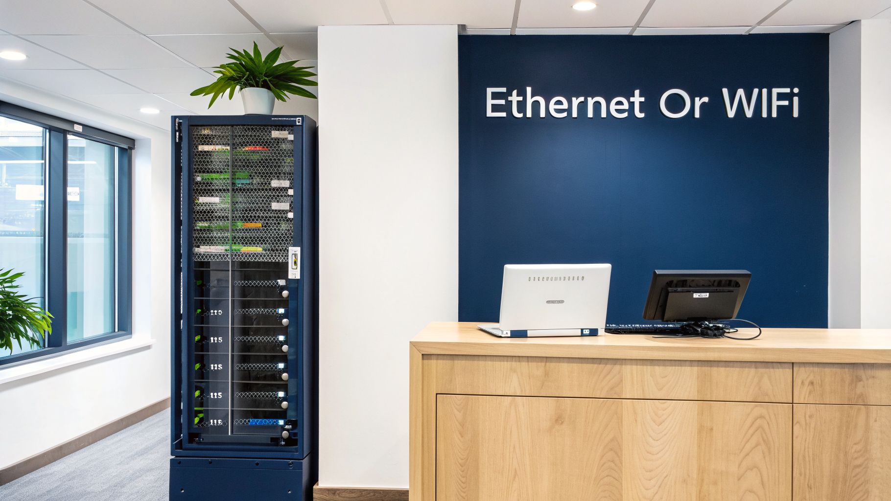 Modern office setup featuring a server rack, a wooden desk with a laptop, and an 'Ethernet Or WiFi' sign.